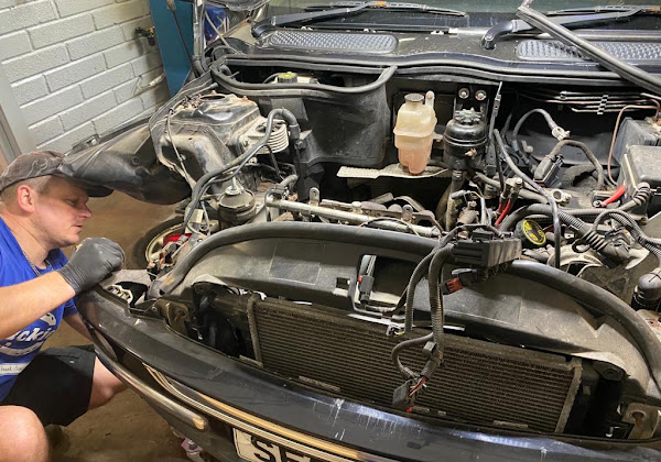 Mechanic working on a car engine with the bumper and radiator removed in the Motortech Dundee workshop